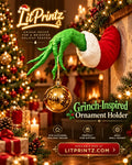 Wall-mounted Grinch-inspired arm holding a gold ornament beside a Christmas tree and fireplace