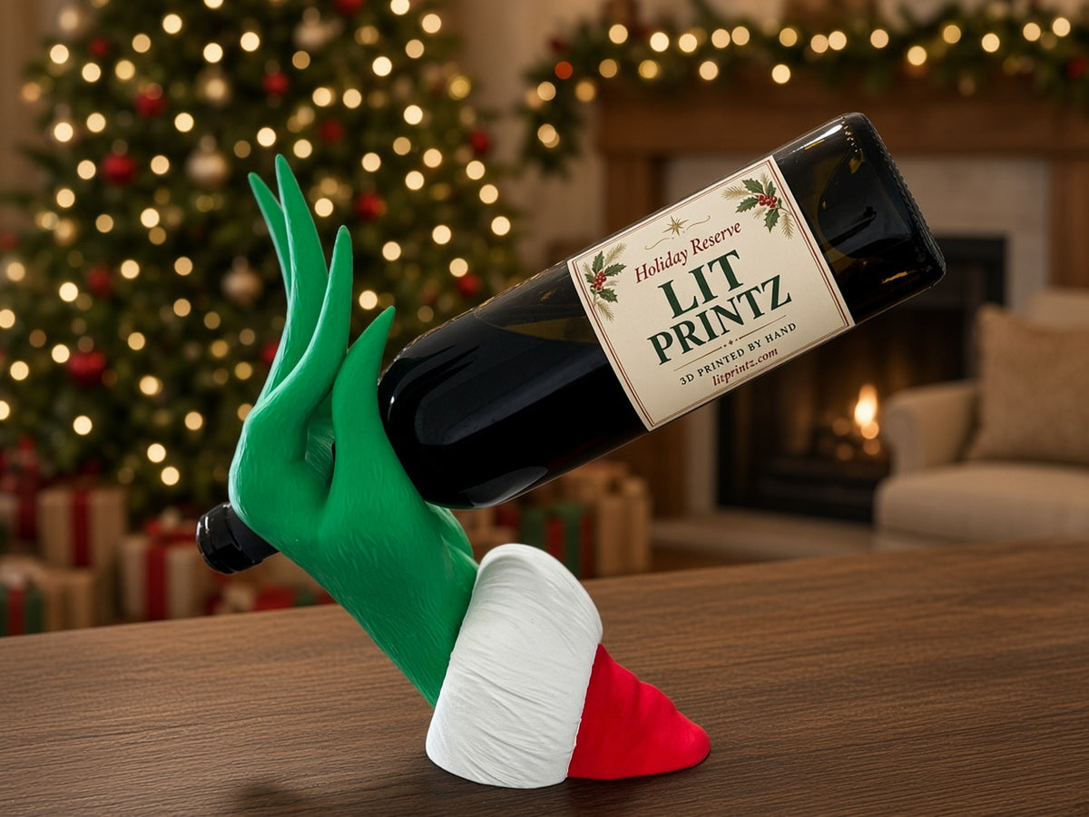 Green Grinch hand wine bottle holder with a white and red Santa cuff, holding a bottle in front of a Christmas tree